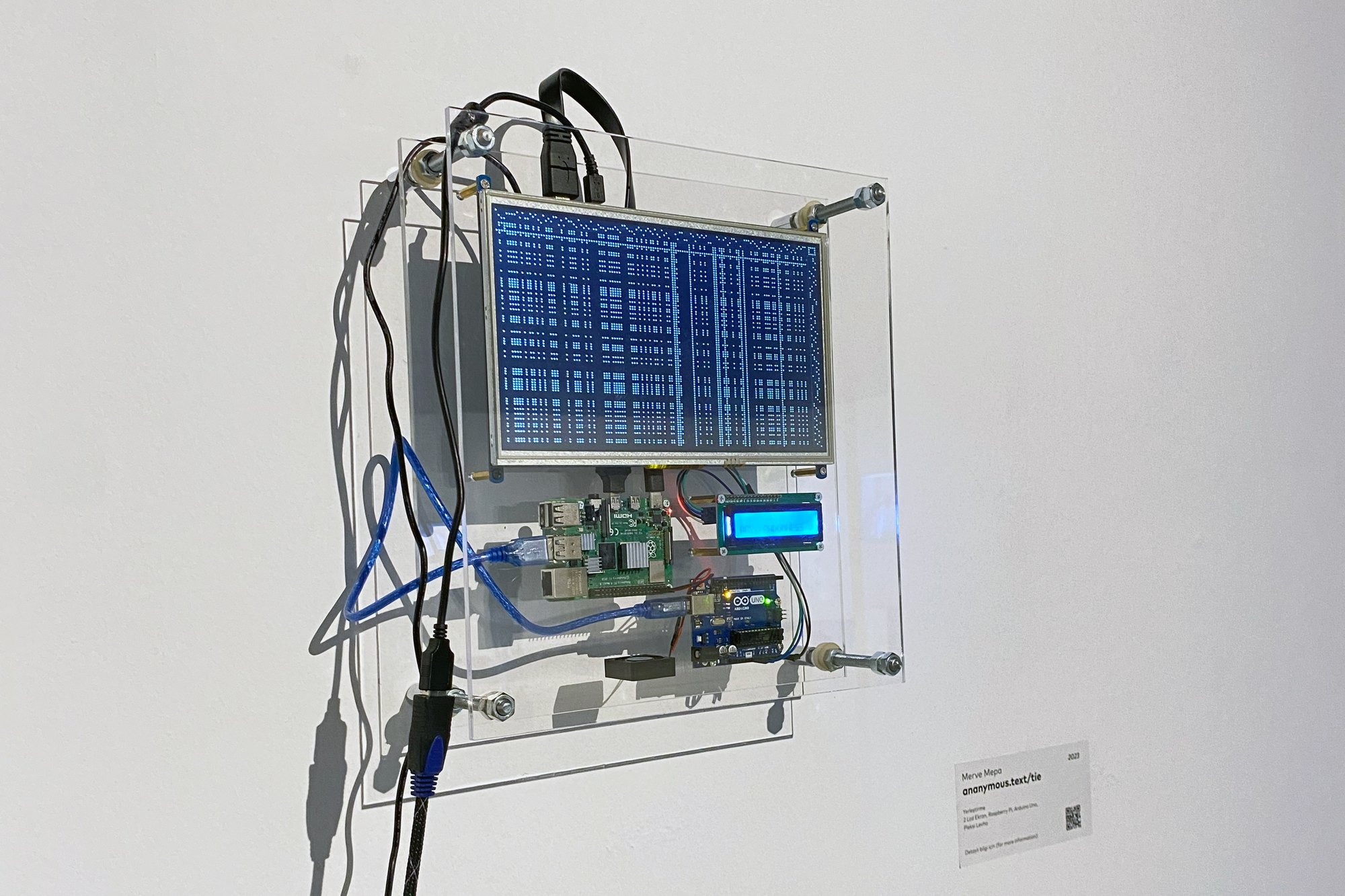 Installation view: a wall-mounted sandwich of acrylic panels holding a 10.1-inch LCD that displays a blue woven draft pattern, with a Raspberry Pi, an Arduino Uno and a small character LCD below it, and cables running down the wall