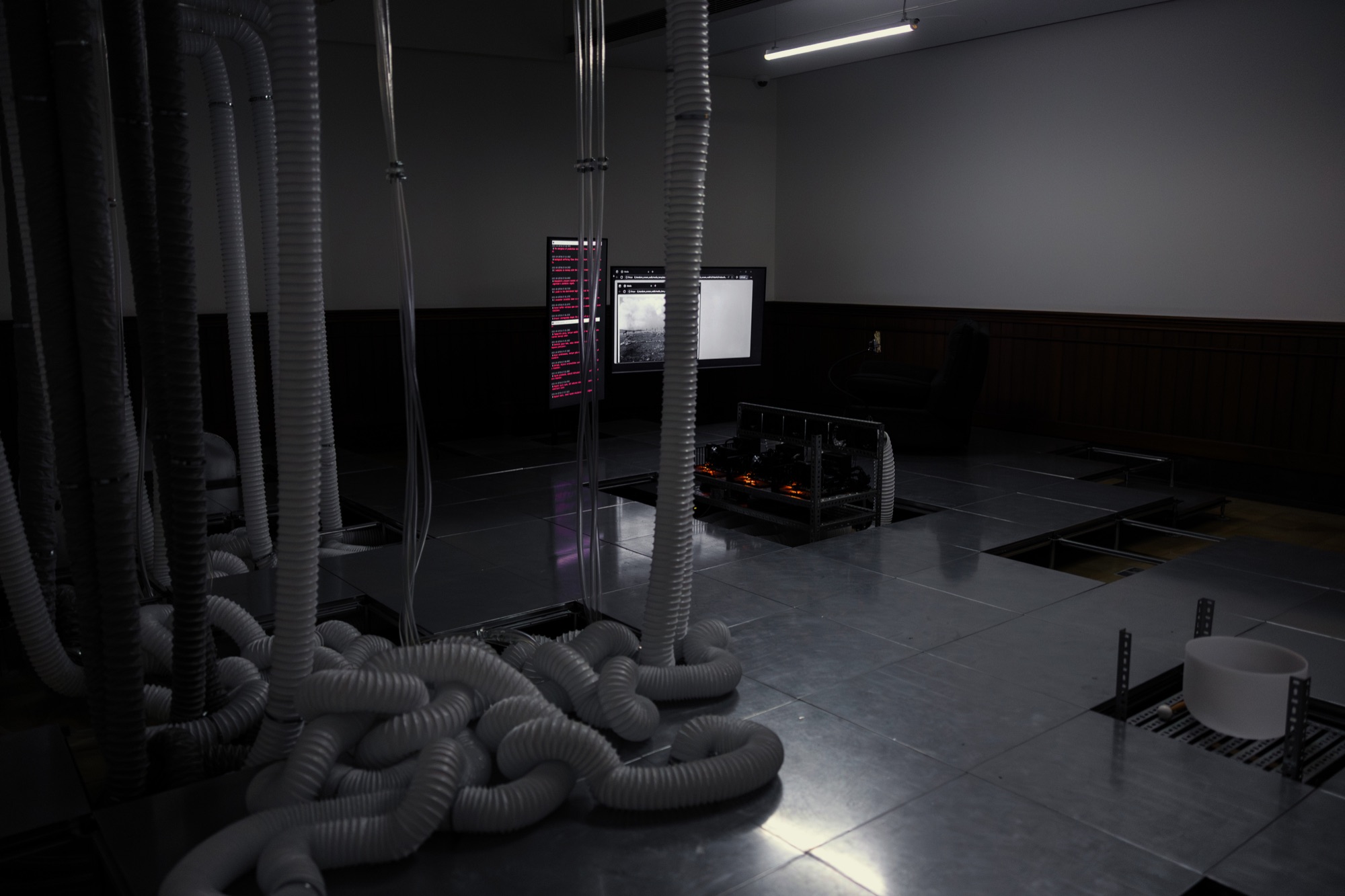 Installation view: white flexible ducts piled on a raised floor with open panels, monitors and equipment beyond